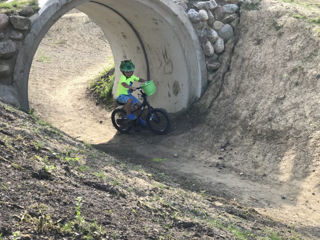 Little boy on bike in fluorescent yellow shirt with green dinosaur helmet biking at Mary Gibbard Park's bike trail.