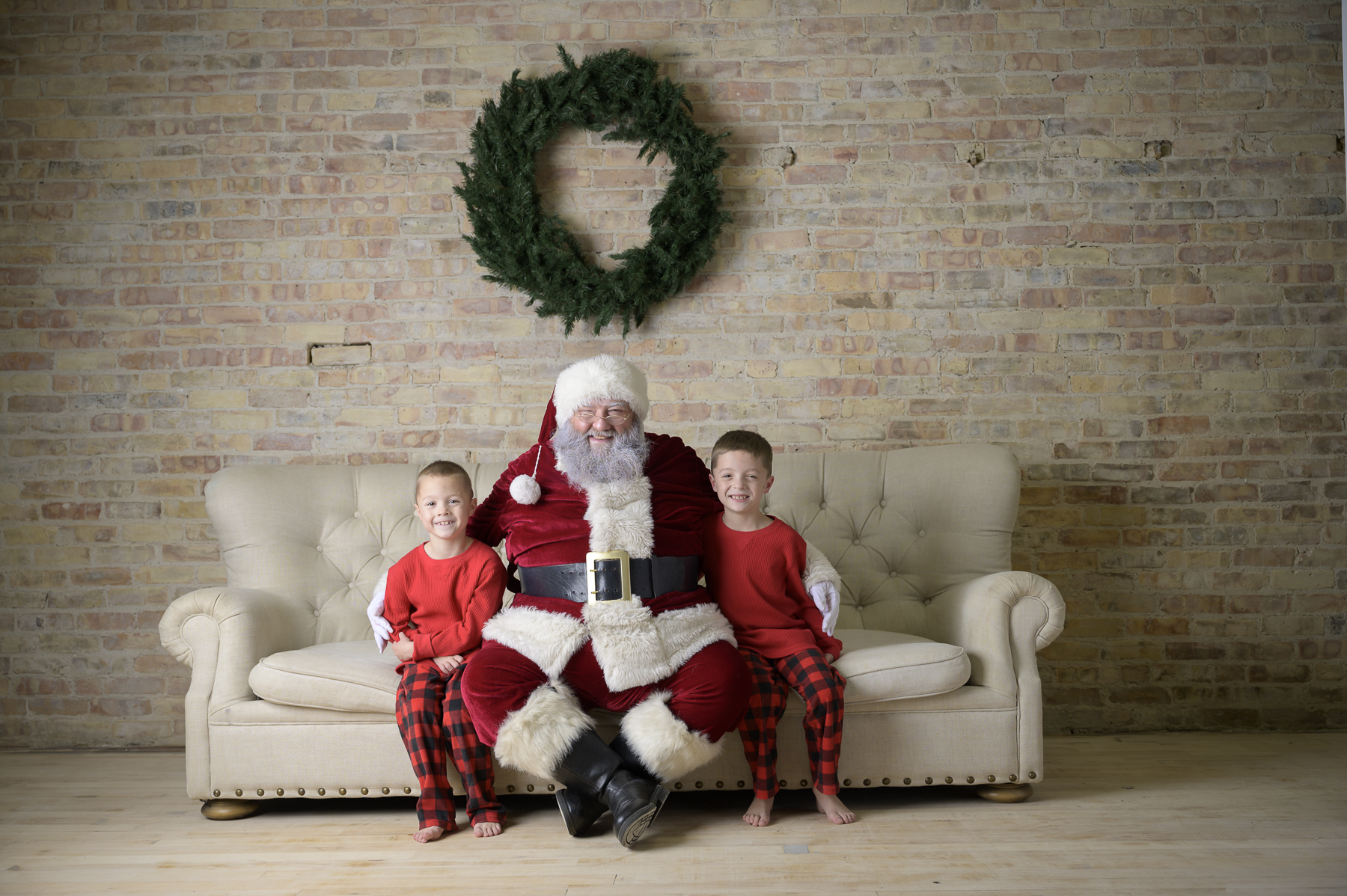 Little boys sitting with Santa on a vintage couch with a wreath on the wall at Always Images in Plymouth Indiana