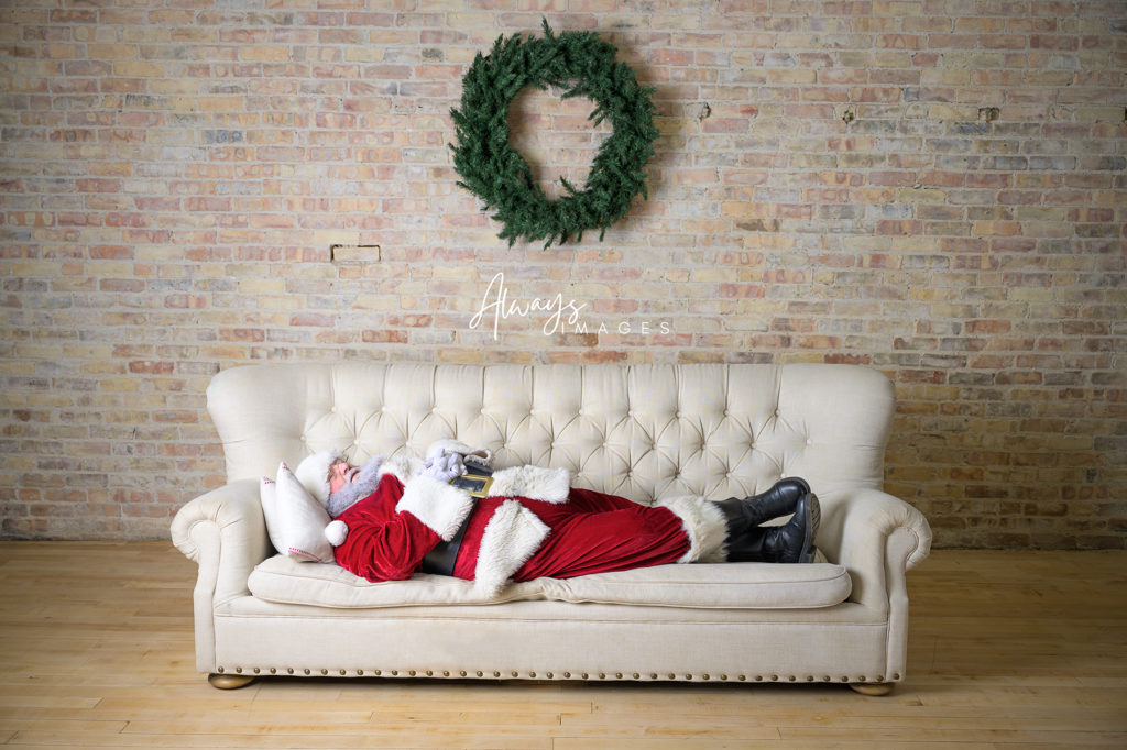 Santa sleeping on a couch with a wreath behind him . 