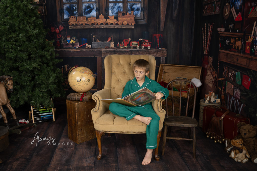 Boy in green pajamas reading The Night Before Christmas in a chair in Santa's Workshop.