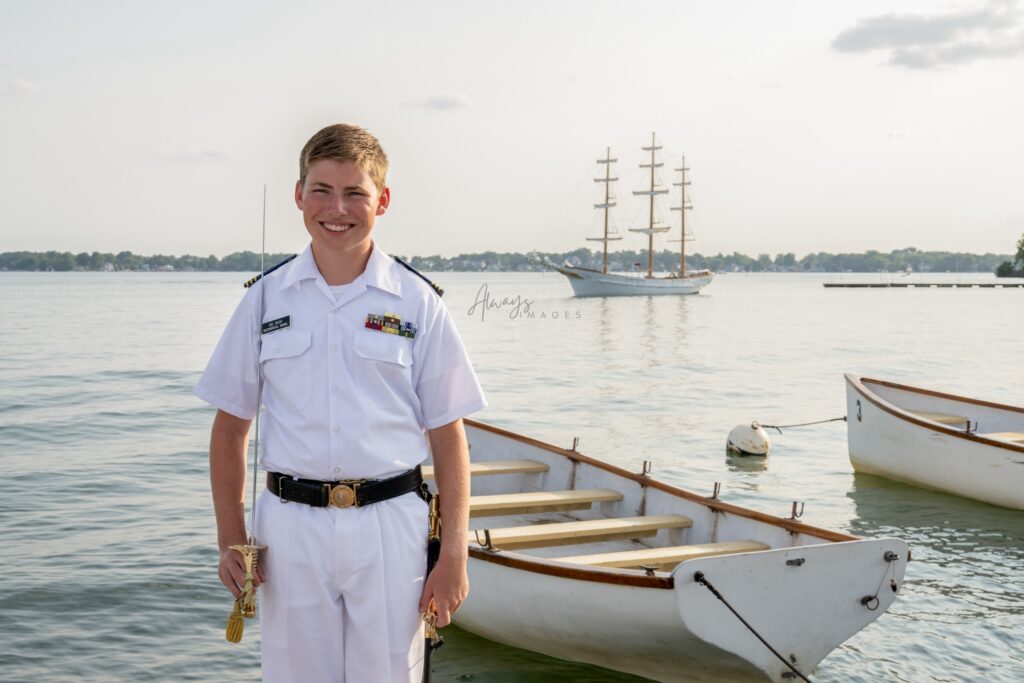 Culver Upper Camp boy in white dress A uniform holding saber with the Ledbetter on Lake Maxinkuckee. 